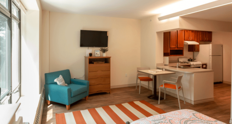 Studio apartment with modern stable supportive housing furniture, including a kitchen, table, chair, and cozy seating area.